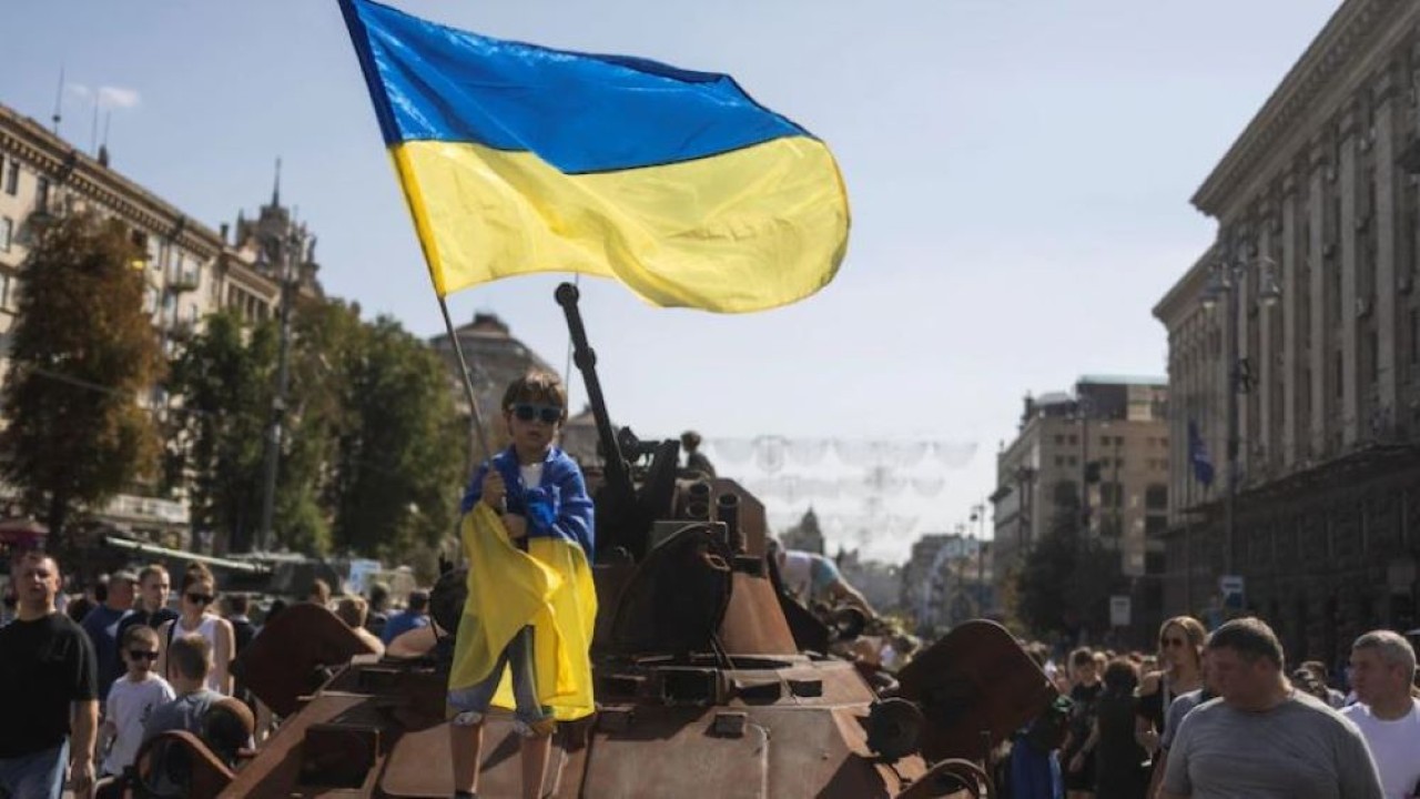 Seorang anak laki-laki mengibarkan bendera nasional Ukraina di atas kendaraan pribadi lapis baja di sebuah pameran kendaraan dan senjata militer Rusia yang hancur. (Valentyn Ogirenko/Reuters)