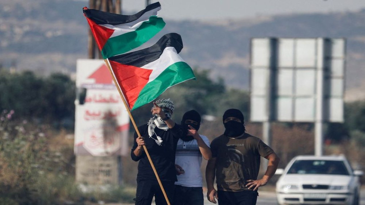 Warga Palestina memegang bendera Palestina selama protes atas ketegangan di Masjid Al-Aqsa Yerusalem, di pos pemeriksaan Huwara, dekat Nablus di Tepi Barat yang diduduki Israel, pada 29 Mei 2022. (Raneen Sawafta/Reuters)