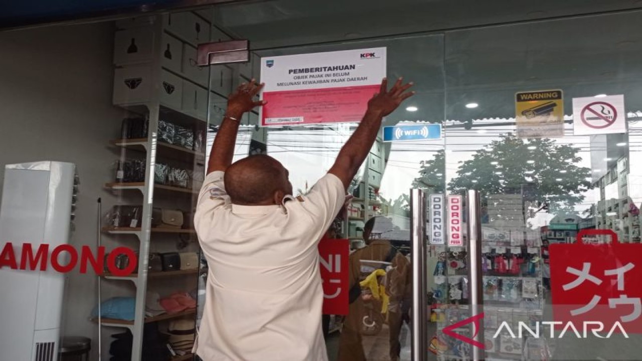 Seorang petugas Bapenda Manokwari memasang stiker berlogo KPK di Toko Samono, Miniso Grup, di Kelurahan Padarni, Distrik Manokwari Barat, Senin (14/11/2022). (ANTARA/Rachmat Julaini)