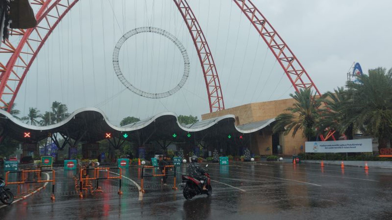 Seorang pengendara sepeda motor melintasi depan pintu gerbang barat Taman Impian Jaya Ancol saat hujan di Jakarta Utara pada Rabu (28/12/2022). ANTARA/Abdu Faisal