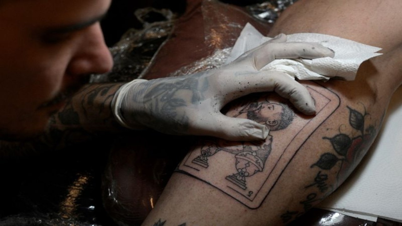 Seniman tato Tebi Cobra Vucinovich asal Argentina mengerjakan tato bergambar kapten tim nasional Argentina Lionel Messi mencium trofi Piala Dunia FIFA di kaki Ariel Sacchi di Ds Tatto Shop, Buenos Aires, Argentina. (23/12/2022) (AFP/JUAN MABROMATA)