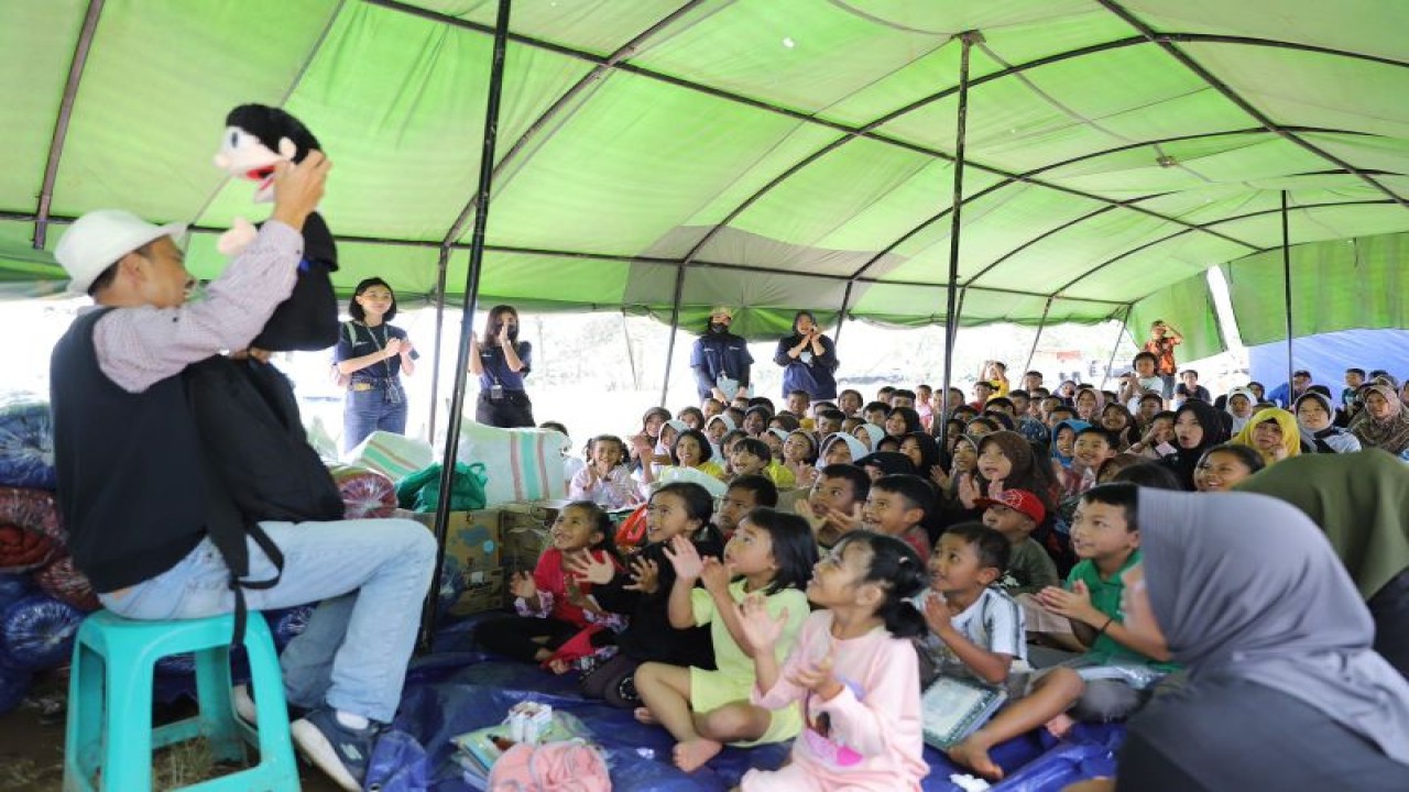Para korban gempa Cianjur menyaksikan pendongeng dengan julukan Mr PRET dalam kegiatan “Forum Humas BUMN untuk Cianjur (Everyone Is A Hero)” di Desa Sukamulya, Cianjur, Jawa Barat, Minggu (18/12/2022). ANTARA/HO-FHBUMN