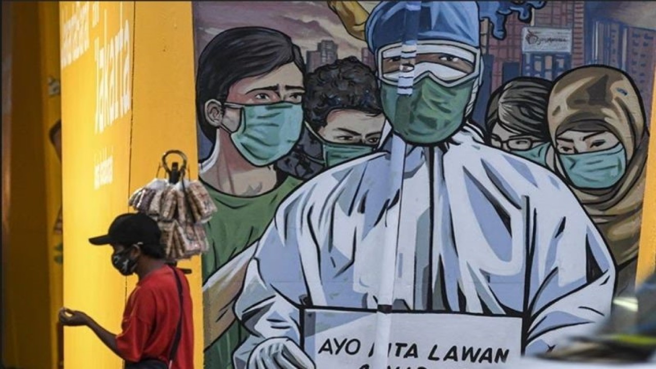 Seorang pedagang yang mengenakan masker melintas di depan mural imbauan untuk melawan COVID-19 di Jakarta, Ahad (29/11/2020). (ANTARA FOTO/M Risyal Hidayat/aww)