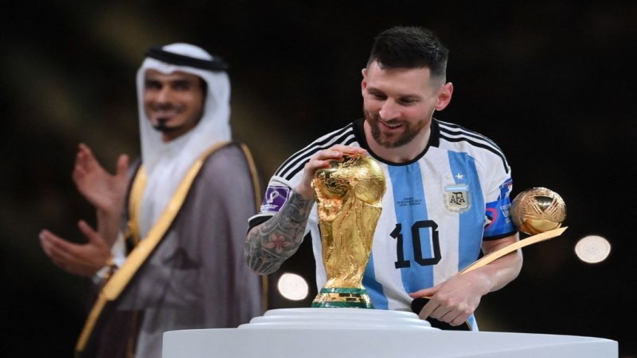 Pemain Argentina Lionel Messi menyentuh trofi Piala Dunia sembari memegang anugerah Bola Emas dalam seremoni penyerahan trofi Piala Dunia setelah final Argentina melawan Prancis di Stadion Lusail, utara Doha, Qatar, pada  18 Desember 2022. (Photo by FRANCK FIFE / AFP) (AFP/FRANCK FIFE)