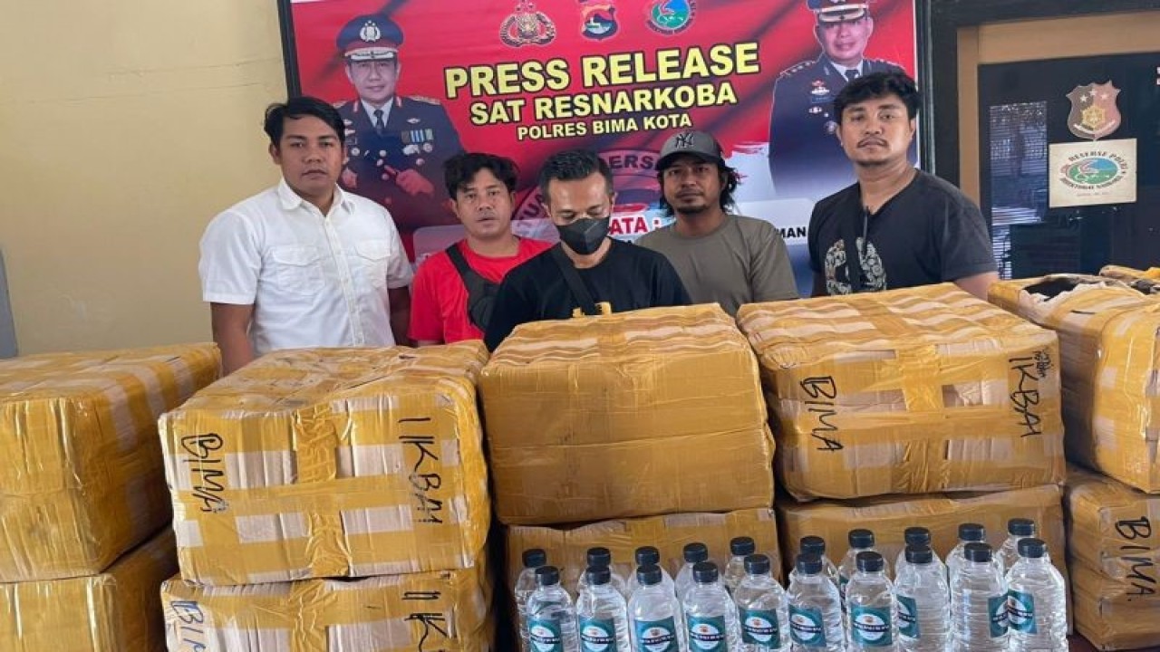 Petugas kepolisian berseragam bebas menunjukkan barang bukti dus dan botol air mineral ukuran tanggung berisi minuman keras tradisional arak khas Bali dengan pemilik berinisial IA di Polres Bima Kota, NTB, Kamis (8/12/2022). (ANTARA/HO-Polres Bima Kota)