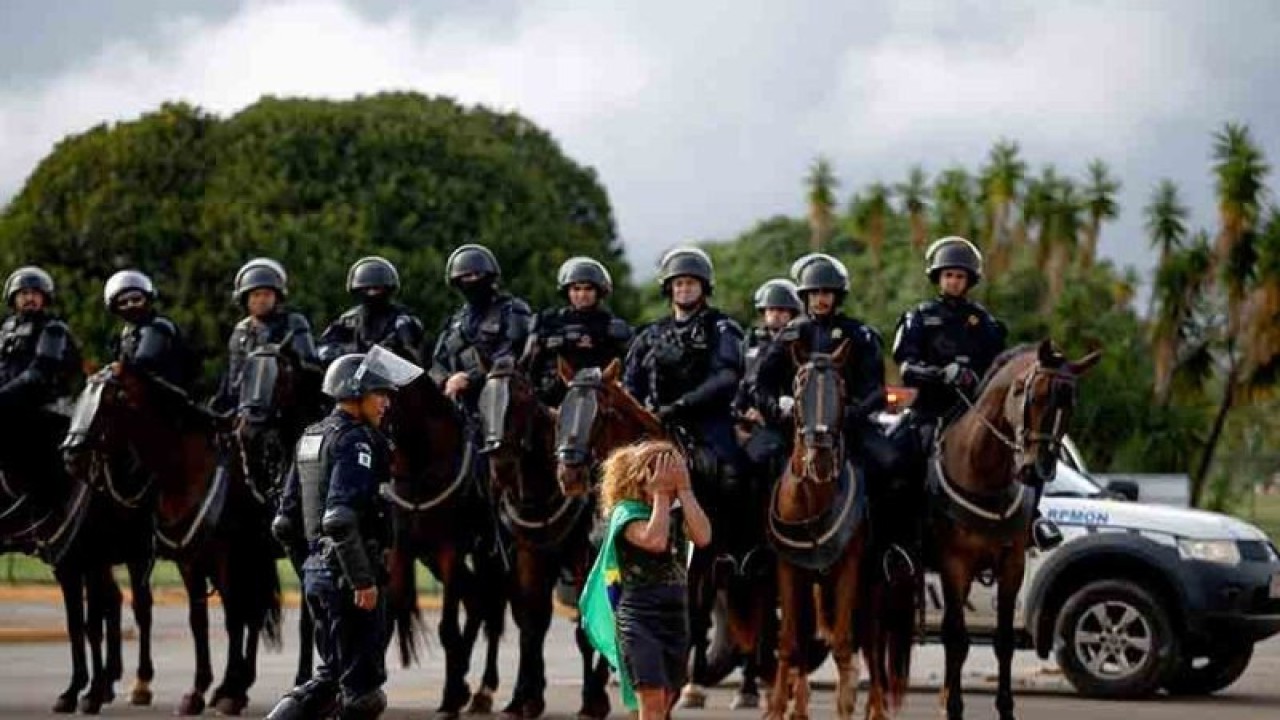 Seorang demonstran berjalan di depan anggota pasukan keamanan di luar Markas Besar Angkatan Darat, di Brasilia, Brasil,Senin (9/1/2023). Aksi ekstrem pengunjuk rasa dilakukan oleh pendukung mantan Presiden Brasil Jair Bolsonaro yang menolak kemenangan Lula. ANTARA FOTO/REUTERS/Amanda Perobelli/rwa.