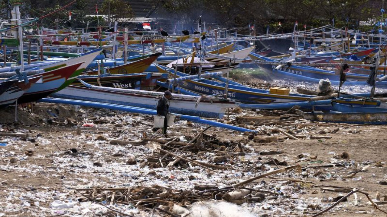 Nelayan melintas di dekat tumpukan sampah saat mengangkut air di Pantai Kedonganan, Badung, Bali, Jumat (13/1/2023). Sampah kiriman yang terdampar di pesisir pantai akibat cuaca ekstrem tersebut menyebabkan aktivitas nelayan terhambat sehingga tidak bisa melaut. ANTARA FOTO/Nyoman Hendra Wibowo/foc.