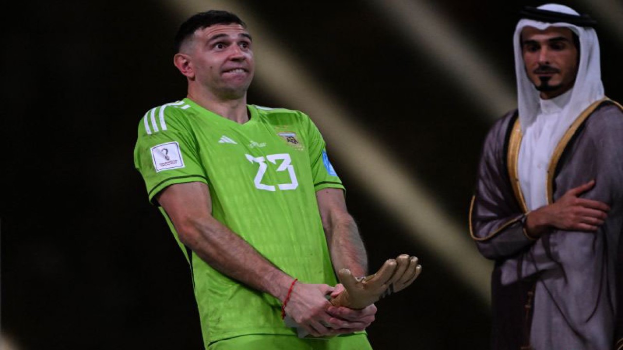 Kiper tim nasional Argentina, Emiliano Martinez (kiri), melakukan selebrasi dengan pose kontroversial bersama trofi Sarung Tangan Emas yang diperolehnya seusai membantu La Albiceleste menjuarai Piala Dunia 2022 seusai mengalahkan Prancis dalam partai final di Stadion Lusail, Al Daayen, Qatar, Sabtu (18/12/2022). (AFP/KIRILL KUDRYAVTSEV)