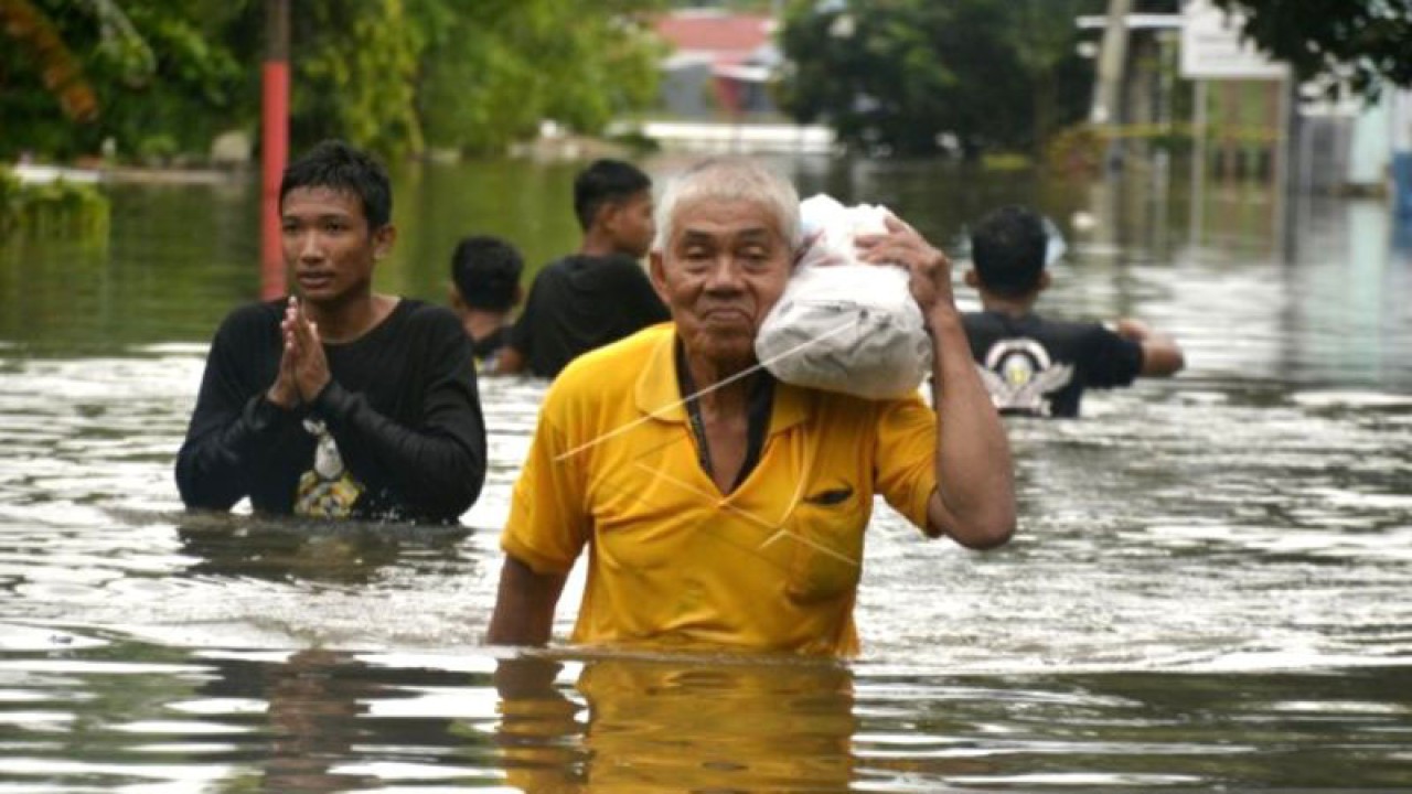 Warga membawa barangnya saat menyeberangi jalan yang tergenang banjir di Kecamatan Manggala, Makassar, Sulawesi Selatan, Minggu (25/12/2022). ANTARA FOTO/Abriawan Abhe.