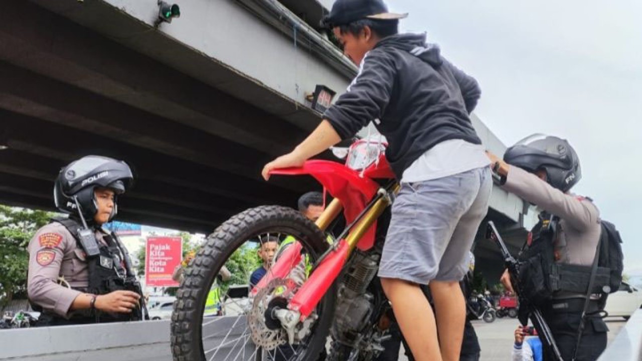 Petugas kepolisian membantu seorang remaja peserta konvoi menaikkan motornya di mobil bak terbuka untuk dibawa ke Kantor Polrestabes Makassar usai ditangkap saat konvoi di bawah jembatan layang Makassar, Sulawesi Selatan, Jumat (20/1/2023). ANTARA/Darwin Fatir
