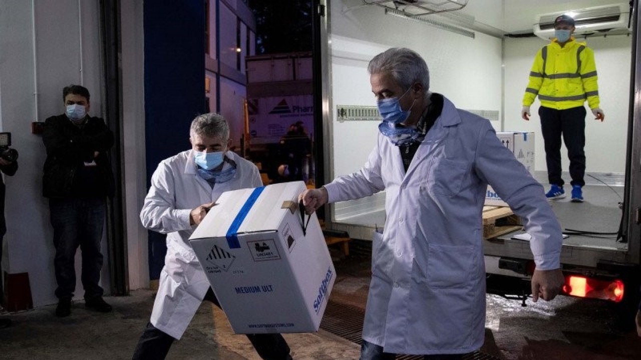Petugas kesehatan membawa kotak berisi vaksin COVID-19 buatan Pfizer-BioNTech saat tiba untuk pertama kalinya di Athena, Yunani, Sabtu (26/12/2020). ANTARA FOTO/REUTERS/Alkis Konstantinidis/pras.