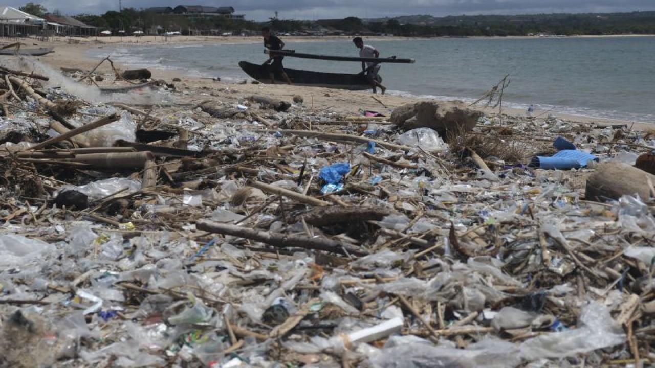 Nelayan mengangkut sampan di dekat tumpukan sampah di Pantai Kedonganan, Badung, Bali, Jumat (13/1/2023). Sampah kiriman yang terdampar di pesisir pantai akibat cuaca ekstrem tersebut menyebabkan aktivitas nelayan terhambat sehingga tidak bisa melaut. ANTARA FOTO/Nyoman Hendra Wibowo/foc.