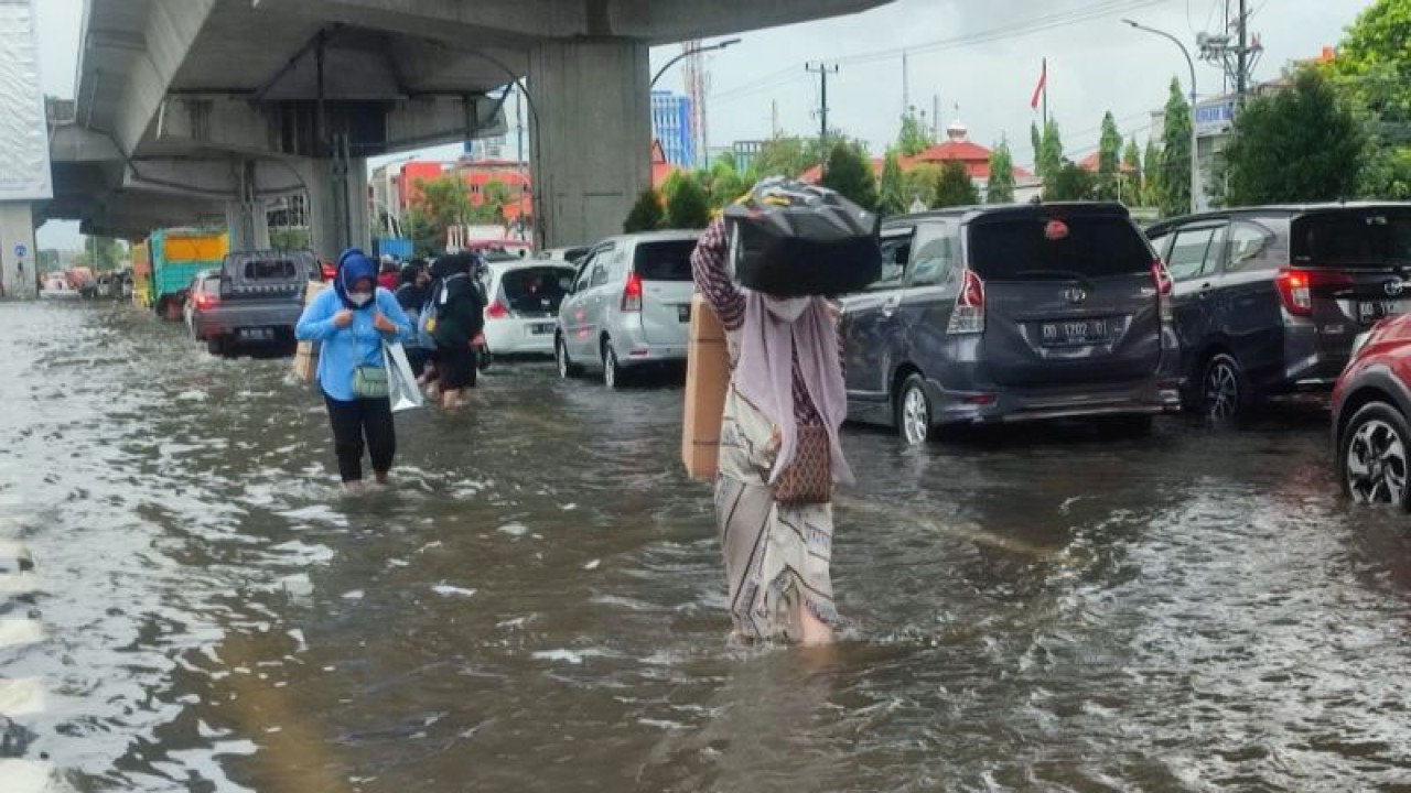 Dua orang pejalan kaki menerobos banjir di jalan protokol Jalan Andi Pangeran Pettarani yang terlihat macet parah saat tergenang air di Makassar, Sulawesi Selatan, Senin (13/2/2023). ANTARA/Darwin Fatir.