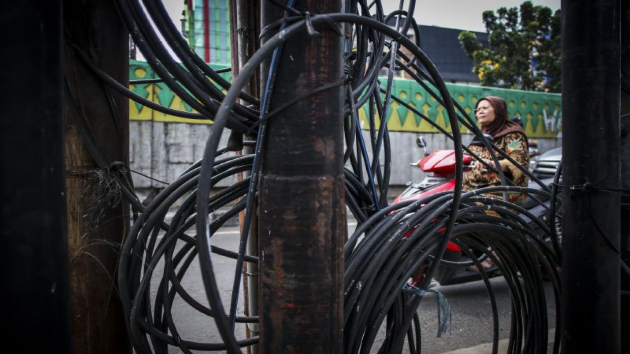 Pengendara melintas di dekat jaringan kabel udara, kawasan Petukangan, Jakarta, Senin (19/12/2022). ANTARA FOTO/Rivan Awal Lingga/aww.