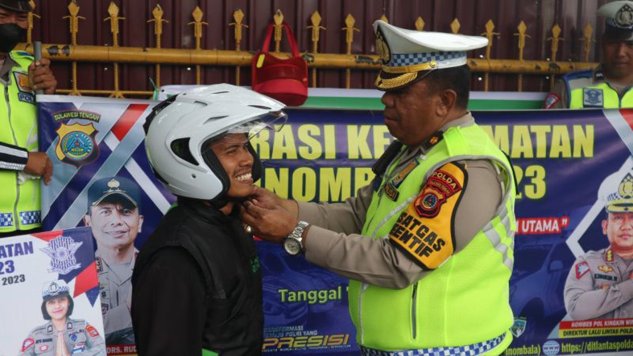 Kasubdit Kamsel Ditlantas Polda Sulteng, Kompol Abubakar Djafar memasang helm kepada seorang pengendara taat berlalu lintas yang diberikan secara gratis pada operasi keselamatan Tinombala 2023 di Jalan Sam Ratulangi, Kota Palu, Senin (13/02/2023). ANTARA/Ditlantas Polda Sulteng