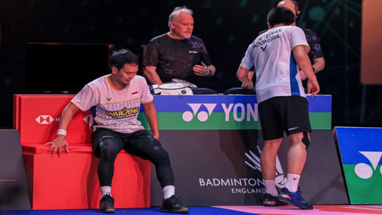 Pebulu tangkis ganda putra Mohammad Ahsan (kiri) duduk di pinggir lapangan usai menerima pemeriksaan tim dokter pertandingan akibat mengalami cedera pada penghujung babak final All England 2023 di Birmingham, Inggris, Minggu. (ANTARA/HO-PP PBSI)