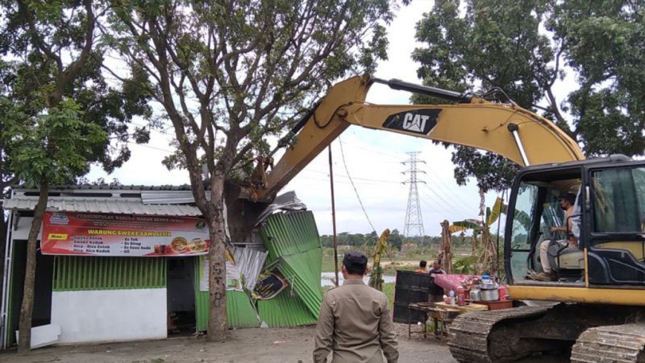 Seorang petugas Satpol PP Kabupaten Kudus, Jawa Tengah, menyaksikan operator excavator merobohkan sebuah warung makan di Jalan Boulevard Lingkar Kencing, Selasa (28/3/2023). Pembongkaran 34 warung makan karena dugaan digunakan untuk transaksi seksual. (ANTARA/Akhmad Nazaruddin Lathif)