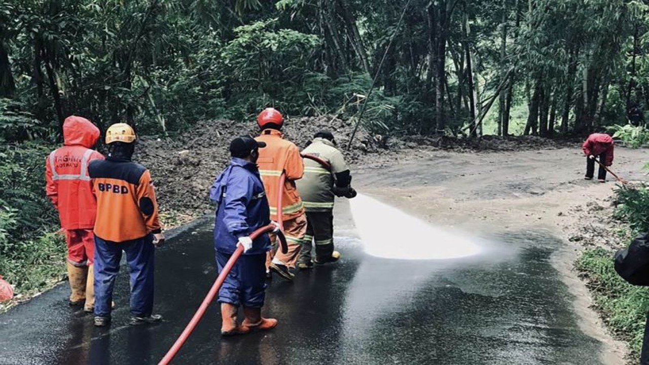 Petugas menyemprotkan air untuk membersihkan sisa material longsor di jalan penghubung Dusun Brau-Dusun Claket, Desa Gunungsari, Kecamatan Bumiaji, Kota Batu, Jawa Timur, Kamis (2/3/2023). (FOTO ANTARA/HO-BPBD Kota Batu)