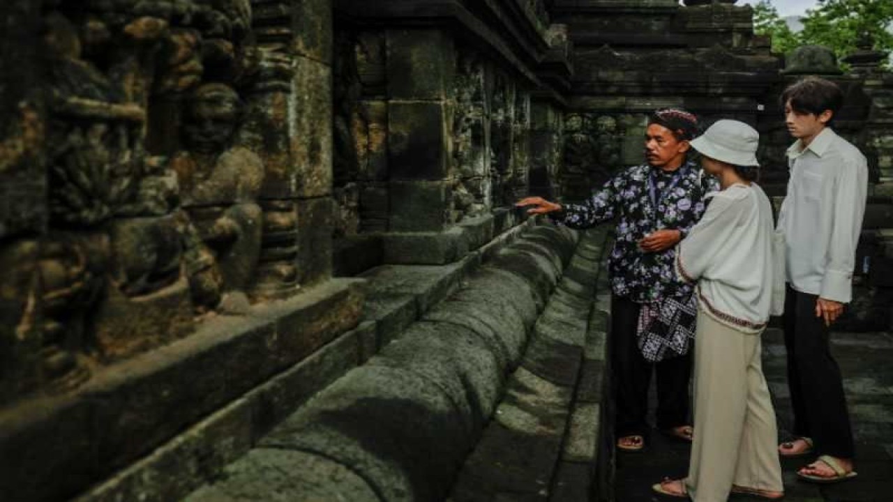 Seorang pemandu dengan pakaian tradisional Jawa menjelaskan isi relief Candi Borobudur kepada wisatawan. ANTARA/HO - PT TWC