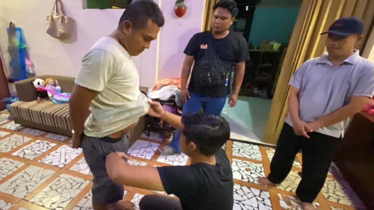 Petugas kepolisian berseragam bebas menggeledah badan YA (kiri) dengan disaksikan aparat lingkungan di rumahnya di wilayah Ampenan, Mataram, NTB, Selasa malam (28/3/2023). (ANTARA/HO-Polresta Mataram)