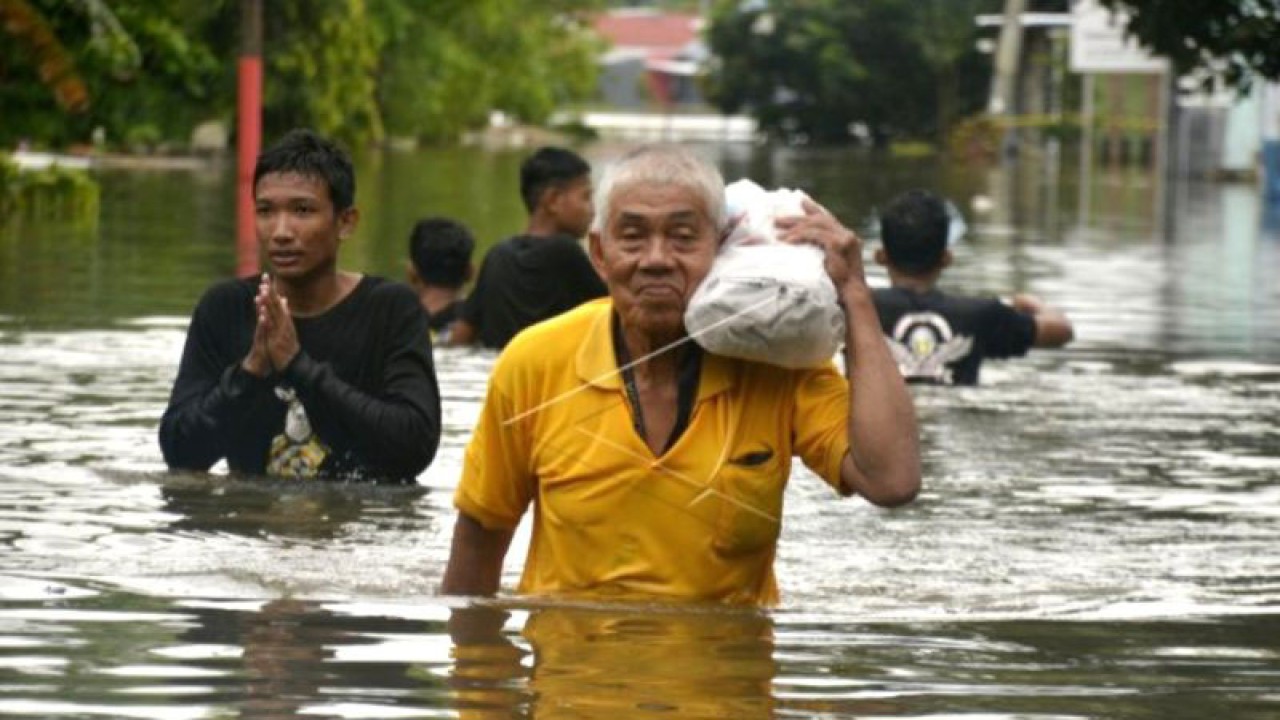 Warga membawa barangnya saat menyeberangi jalan yang tergenang banjir di Kecamatan Manggala, Makassar, Sulawesi Selatan, Minggu (25/12/2022). ANTARA FOTO/Abriawan Abhe.