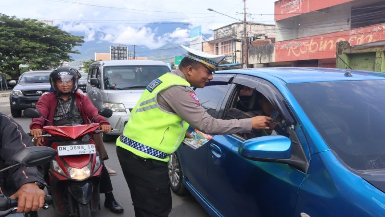 Personel Direktorat Lalu Lintas (Ditlantas) Polda Sulawesi Tengah membagikan brosur tertib lalu lintas di "traffic light" Kota Palu. ANTARA/HO-Ditlantas Polda Sulteng