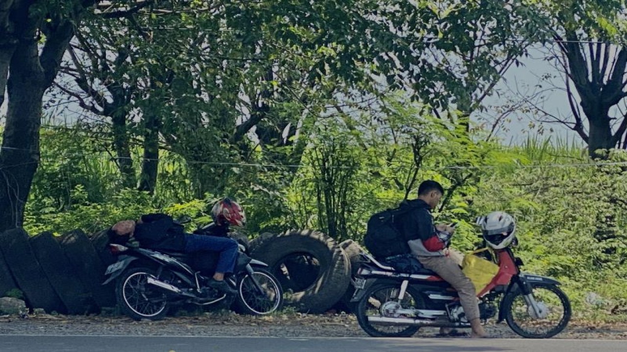 Dua pemudik yang menggunakan motor nampak rehat sejenak di bawah pohon rindang yang ada di sekitar Jalur Pantura, Brebes ke arah Tegal, Jawa Tengah pada Kamis (20/4/2023). (ANTARA/Hreeloita Dharma Shanti)