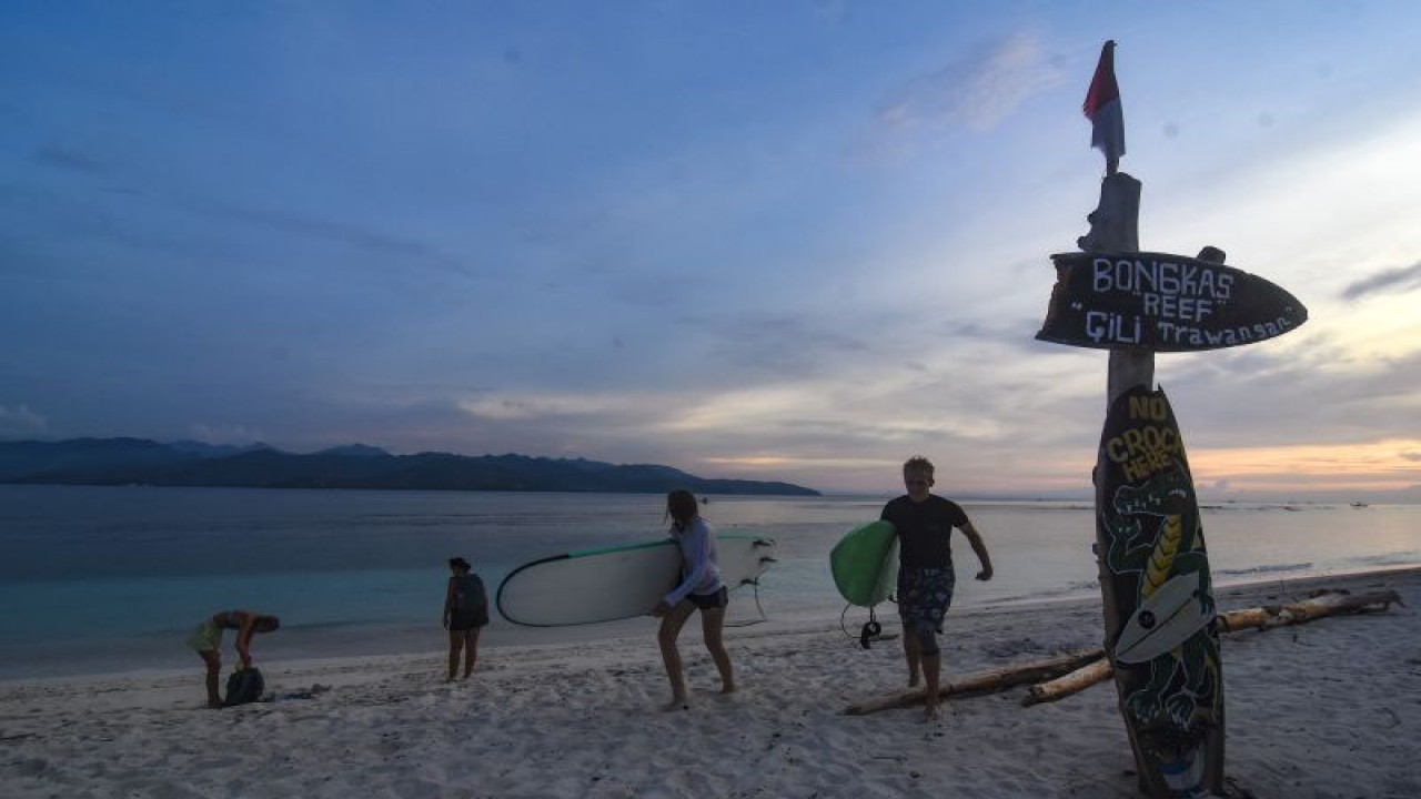 Arsip - Wisatawan asing membawa papan surfing di pinggiran pantai wisata Gili Trawangan, Kecamatan Pemenang, Tanjung, Lombok Utara, NTB, Rabu (14/12/2022). (ANTARA FOTO/Ahmad Subaidi/aww)