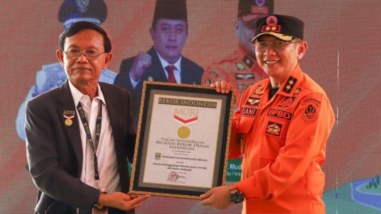 Direktur Operasional MURI Yusuf Ngadri menyerahkan piagam penghargaan pemecahan Rekor MURI kategori simulasi evakuasi bencana dengan peserta terbanyak se-Indonesia kepada Penjabat Bupati Bekasi Dani Ramdan di Situ Binong, Senin. (ANTARA/Pradita Kurniawan Syah).