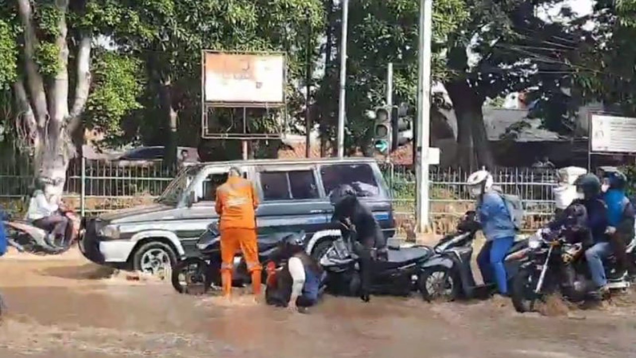 Petugas Penanganan Prasarana dan Sarana Umum (PPSU) tengah membantu pengendara motor yang terjatuh karena meluapnya Kali Baru hingga ke jalan di perempatan Hek, Kramat Jati, Jakarta Timur, Senin (19/6/2023). ANTARA/Syaiful Hakim