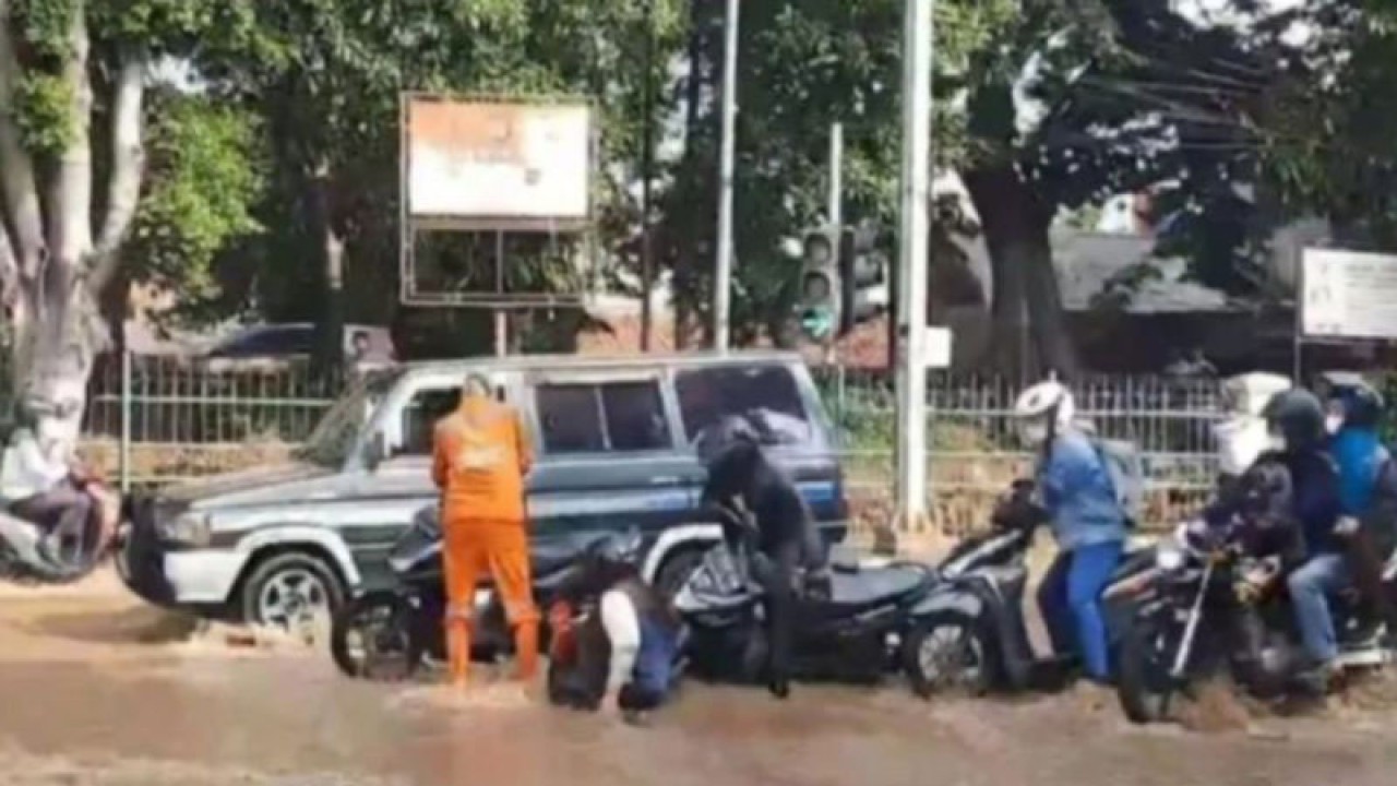 Petugas Penanganan Prasarana dan Sarana Umum (PPSU) tengah membantu pengendara motor yang terjatuh karena meluapnya Kali Baru hingga ke jalan di perempatan Hek, Kramat Jati, Jakarta Timur, Senin (19/6/2023). ANTARA/Syaiful Hakim