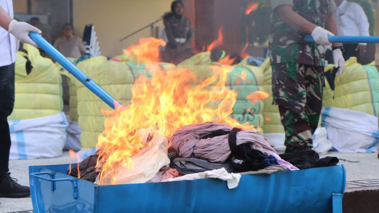 petugas kepolisian dan TNI membakar pakaian bekas impor dalam kegiatan pemusnahan barang bukti sitaan kasus thrifting di Lapangan Bhara Daksa Polda NTB, Mataram, Senin (8/5/2023). (ANTARA/Dhimas B.P.)