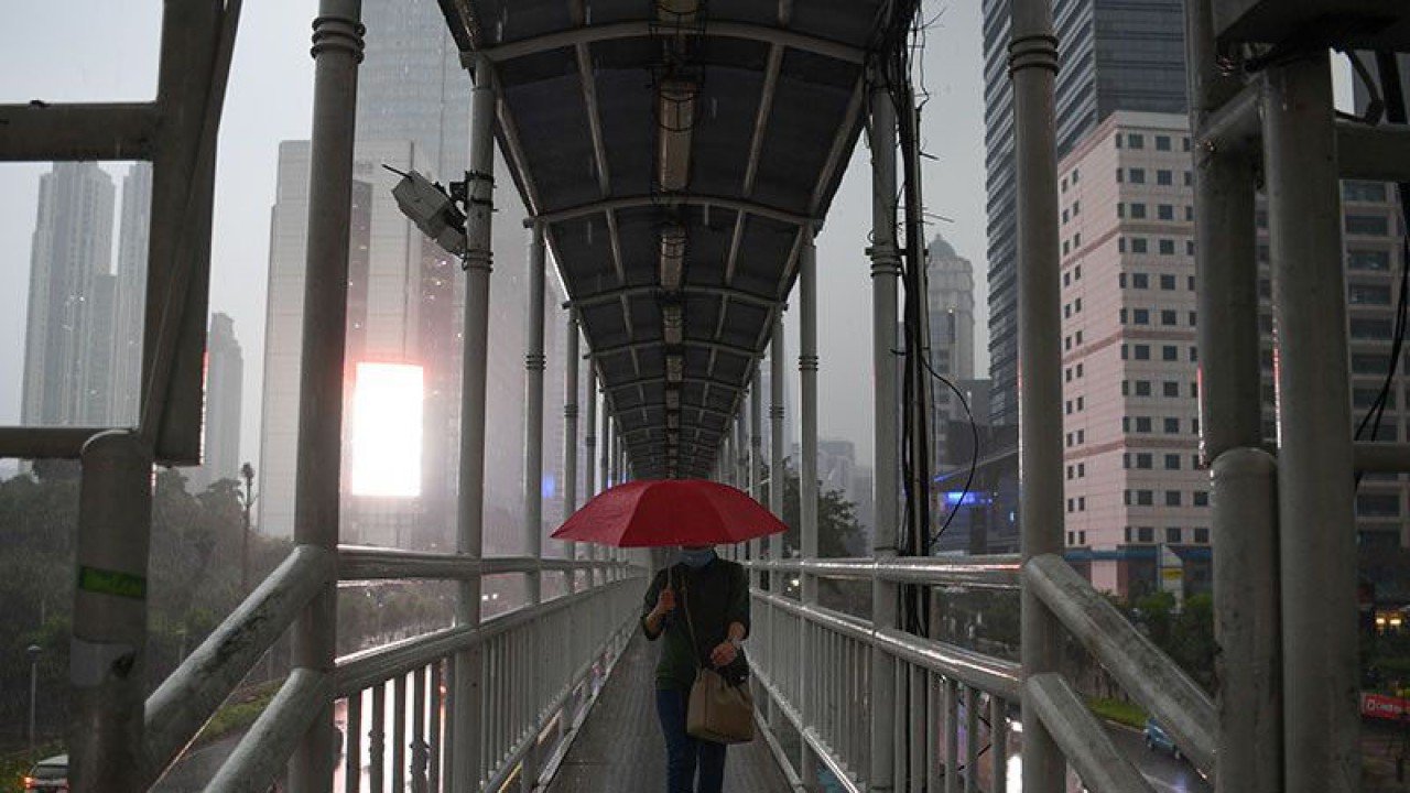 Aesip foto - Seorang warga membawa payung saat melintas di jembatan penyeberangan orang (JPO) di Jalan Jenderal Sudirman, Jakarta, Jumat (16/10/2020). ANTARA FOTO/Wahyu Putro A/wsj/pri. (ANTARA FOTO/WAHYU PUTRO A)