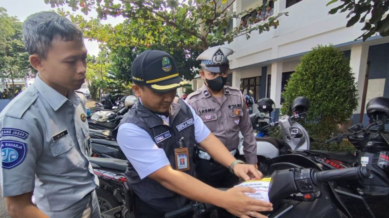 Petugas Samsat Cianjur, Jawa Barat, memasang stiker pemberitahuan jatuh tempo pajak pada kendaraan yang terparkir di area sekolah di Cianjur, Rabu (20/9/2023). ANTARA/Ahmad Fikri
