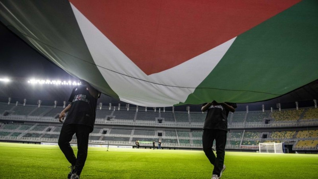 Arsip - Petugas membawa bendera kebangsaan Palestina saat melakukan gladi resik dan latihan tim sepak bola Palestina jelang pertandingan sepak bola persahabatan (FIFA Matchday) antara Timnas Indonesia melawan tim sepak bola Palestina di Stadion Gelora Bung Tomo, Surabaya, Selasa (13/6/2023). ANTARA FOTO/Muhammad Adimaja/foc. (ANTARA FOTO/MUHAMMAD ADIMAJA)