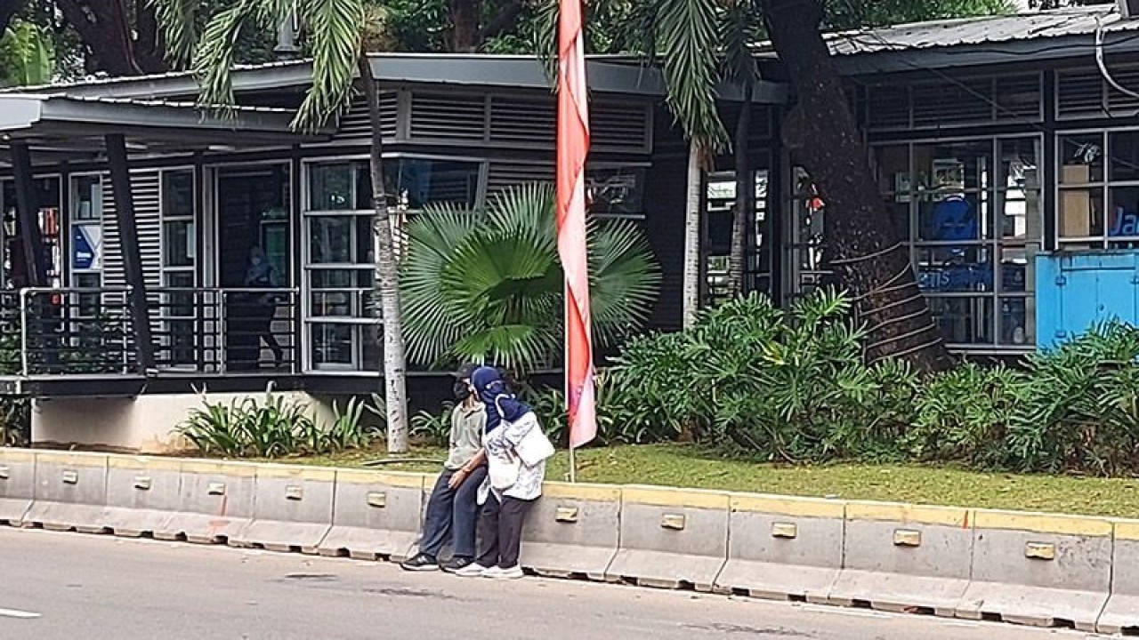 Dua orang duduk di pembatas jalur bus TransJakarta depan Halte Monas yang tidak beroperasi sementara hingga pukul 11.05 WIB saat berlangsung upacara perayaan HUT ke-77 RI di Istana Merdeka, Jakarta Pusat, Rabu (17/8/2022) pagi. ANTARA/Abdu Faisal/aa.
