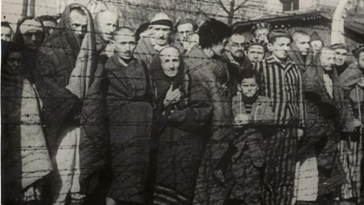 Korban selamat Holocaust berdiri di belakang pagar kawat berduri setelah pembebasan kamp kematian Jerman Nazi Auschwitz-Birkenau pada tahun 1945 di Polandia yang diduduki Nazi. Foto/Arsip Yad Vashem/REUTERS