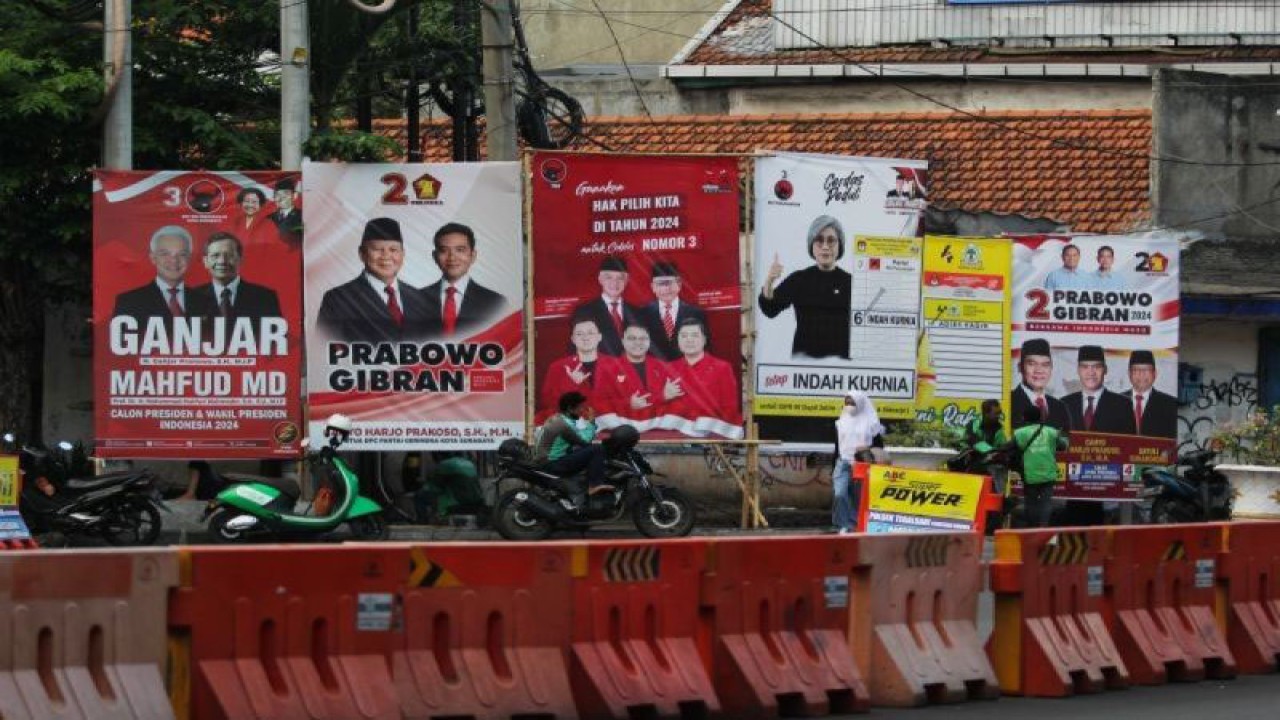 Pelajar berjalan di dekat alat peraga kampanye yang dipasang di persimpangan Jalan Tegalsari-Jalan Basuki Rahmat, Surabaya, Jawa Timur, Selasa (5/12/2023). (ANTARA FOTO/Didik Suhartono/wpa.)