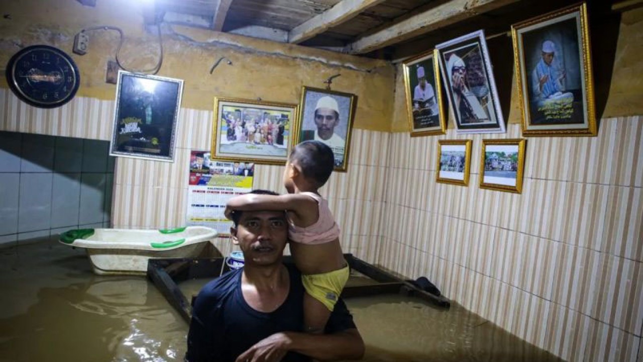 Warga menggendong anak di rumahnya saat banjir melanda di kawasan Kebon Pala, Kampung Melayu, Jakarta, Kamis (30/11/2023). ANTARA FOTO/Erlangga Bregas Prakoso/aww.