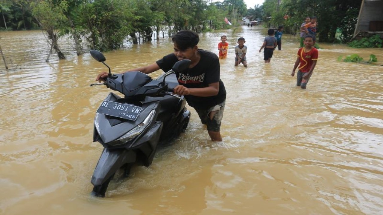 Arsip Foto - Warga mendorong sepeda motornya saat melintasi jalanan yang terendam banjir di Desa Pasi Aceh Tunong, Meureubo, Aceh Barat, Aceh, Selasa (12/12/2023). (ANTARA FOTO/SYIFA YULINNAS)