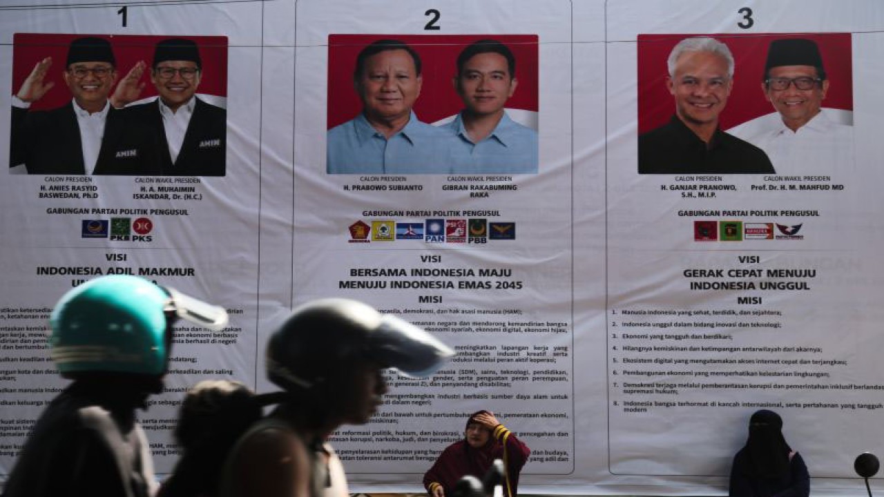 Warga duduk di dekat baliho sosialisasi tiga pasangan calon presiden dan wakil presiden pada Pemilu 2024 yang terpajang di Pasar Barito, Kota Ternate, Maluku Utara, Kamis (14/12/2023). Baliho sosialisasi pilpres tersebut bertujuan untuk mengajak masyarakat agar menggunakan hak pilihnya pada pilpres, 14 Februari 2024. ANTARA FOTO/Andri Saputra/Spt.