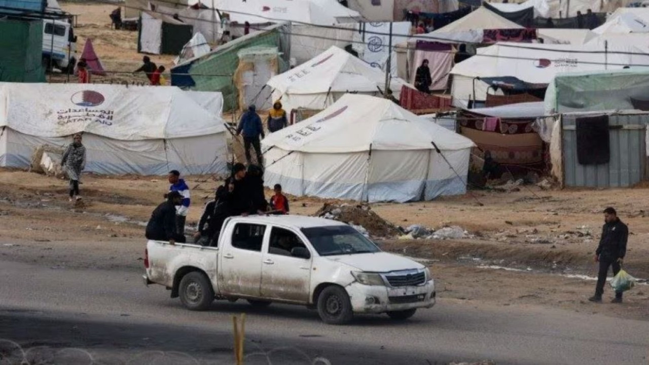 Petugas keamanan yang menjaga truk yang membawa bantuan, berkendara di samping tenda kamp, ​​​​tempat pengungsi Palestina berlindung setelah meninggalkan rumah mereka karena serangan Israel di Rafah, Jalur Gaza selatan, 17 Januari 2024. (Mohammed Salem/Reuters)