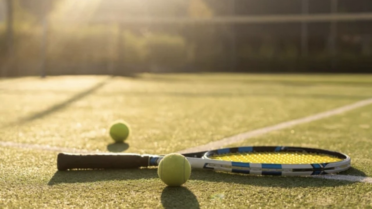 Foto ilustrasi raket tenis dengan bola di lapangan saat matahari hampir terbenam
